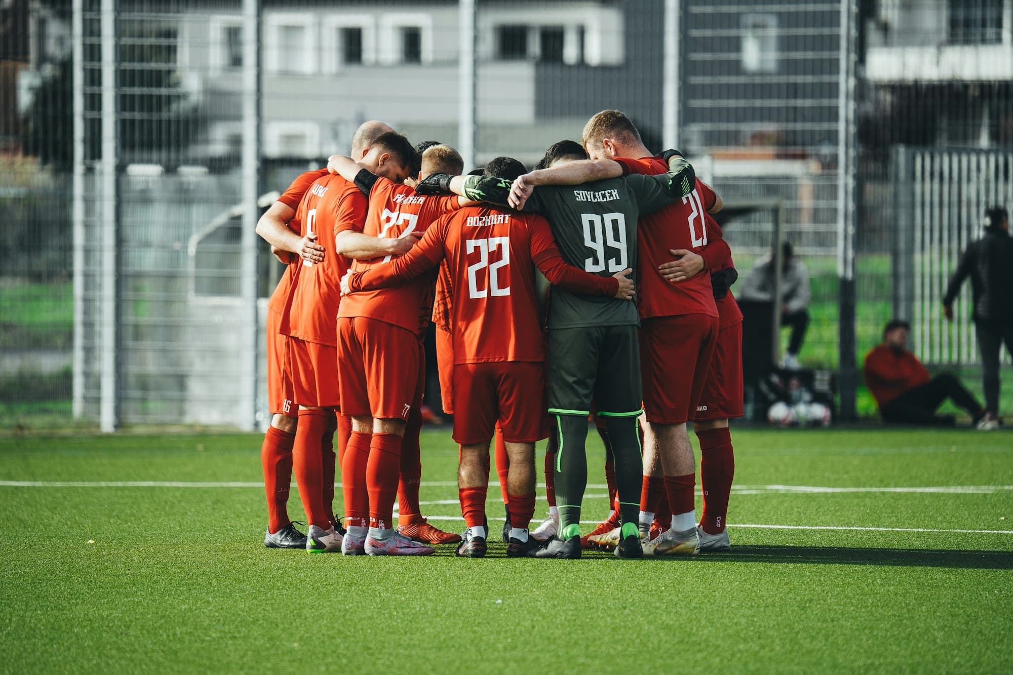 Joueurs de football en cercle, bras sur les épaules, juste avant le coup d’envoi