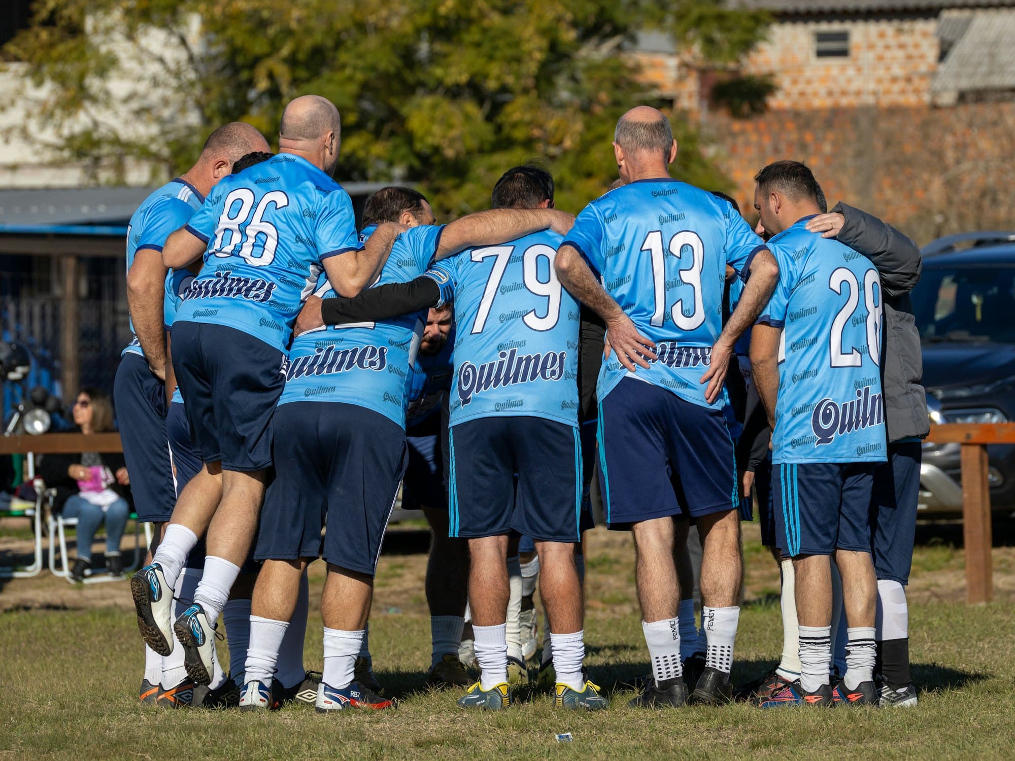 Équipe de vétérans en maillots bleus, rassemblée en cercle avant le match